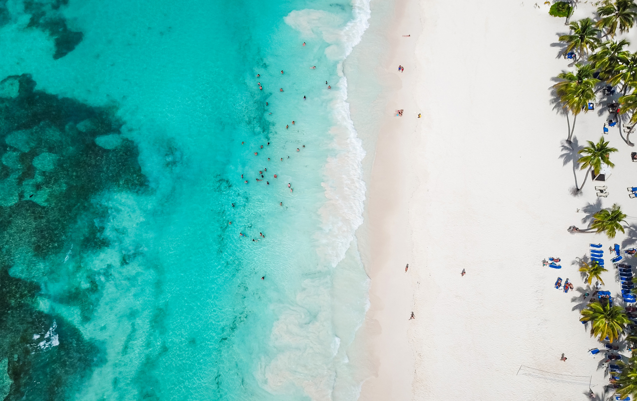 Incredible view of the white sandy beach from a bird’s eye view. Top view of beautiful white sand beach with turquoise sea water and palm trees, aerial drone shot.